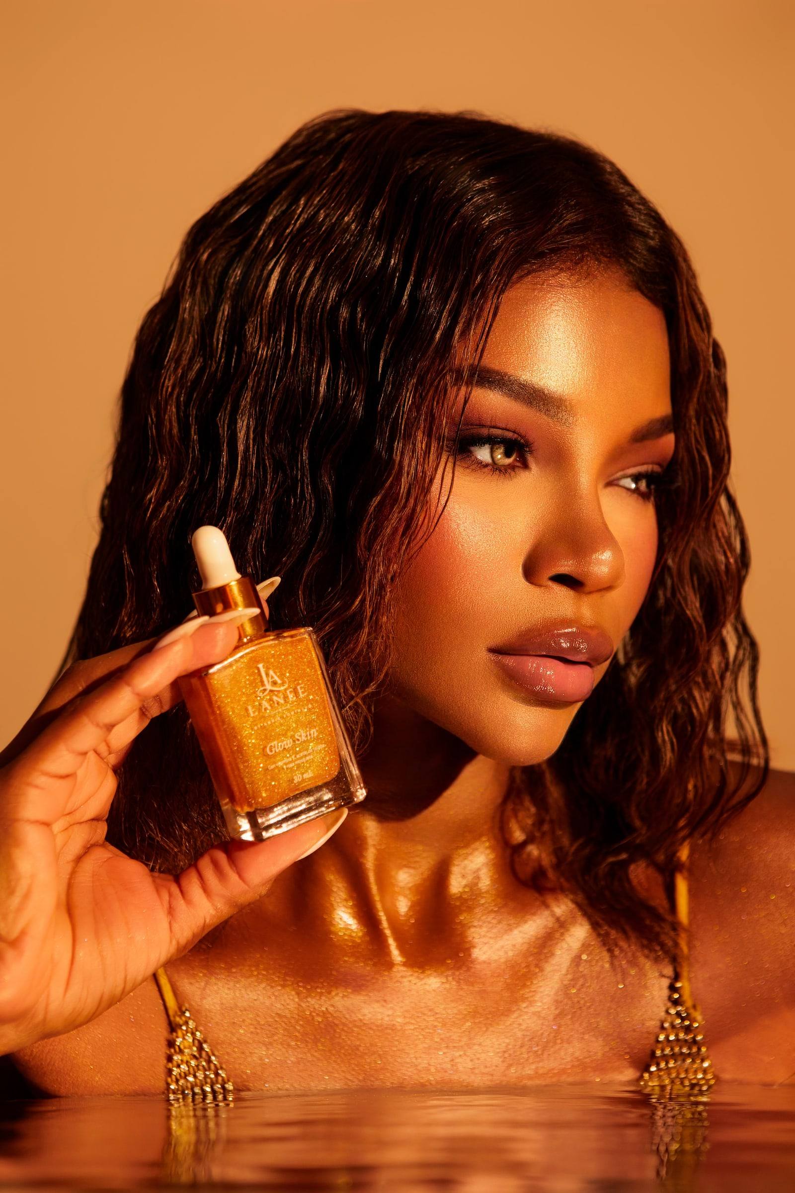 Modelo con la piel iluminada sosteniendo Glow Skin Gold junto a su rostro